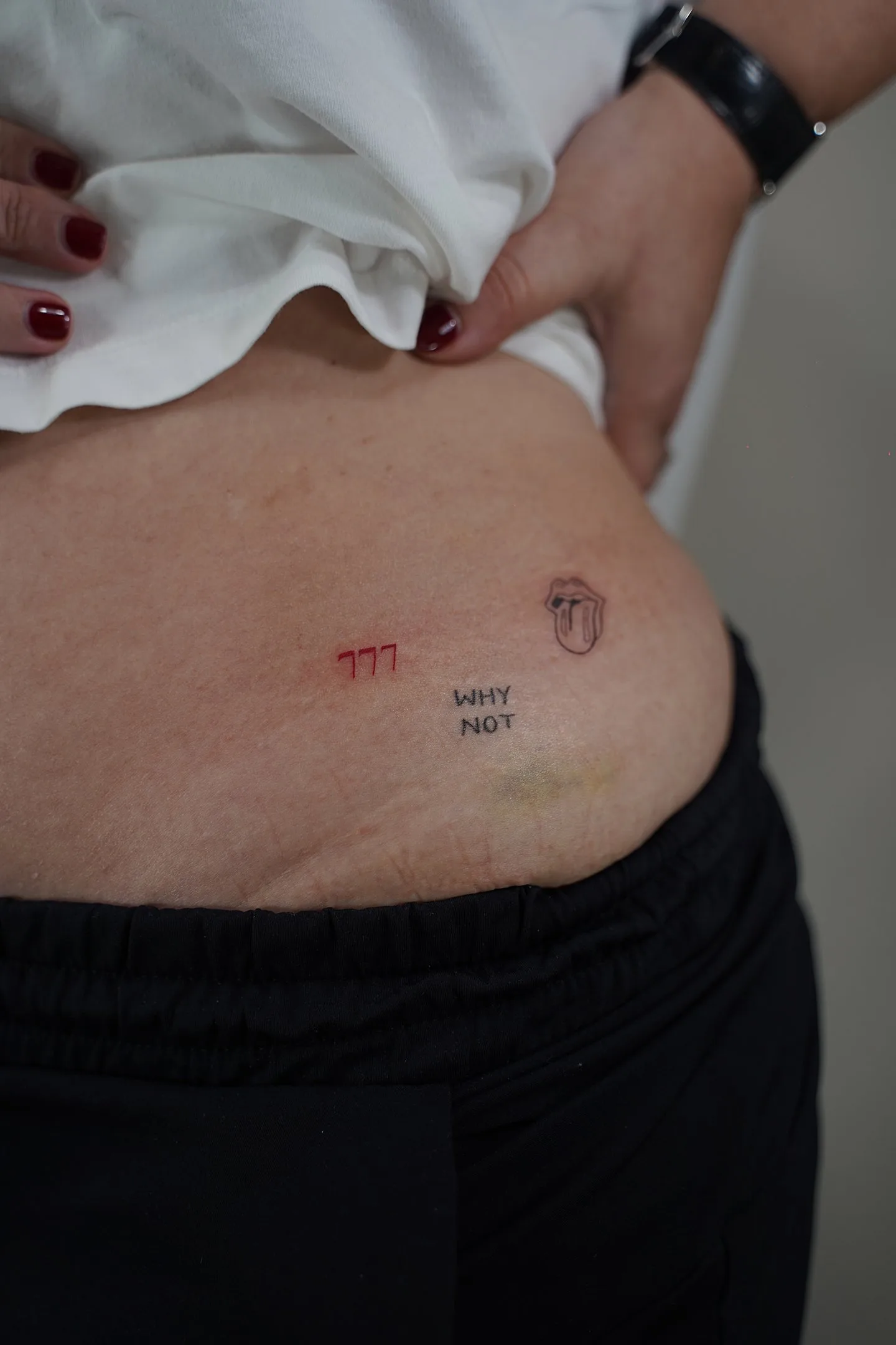 Tatuaje fineline 777 en rojo y boca con lengua en abdomen madrid