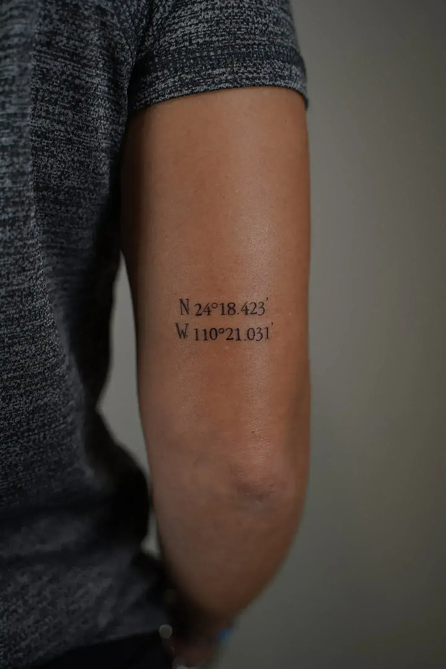 Tatuaje fineline coordenadas geográficas en parte posterior del brazo madrid