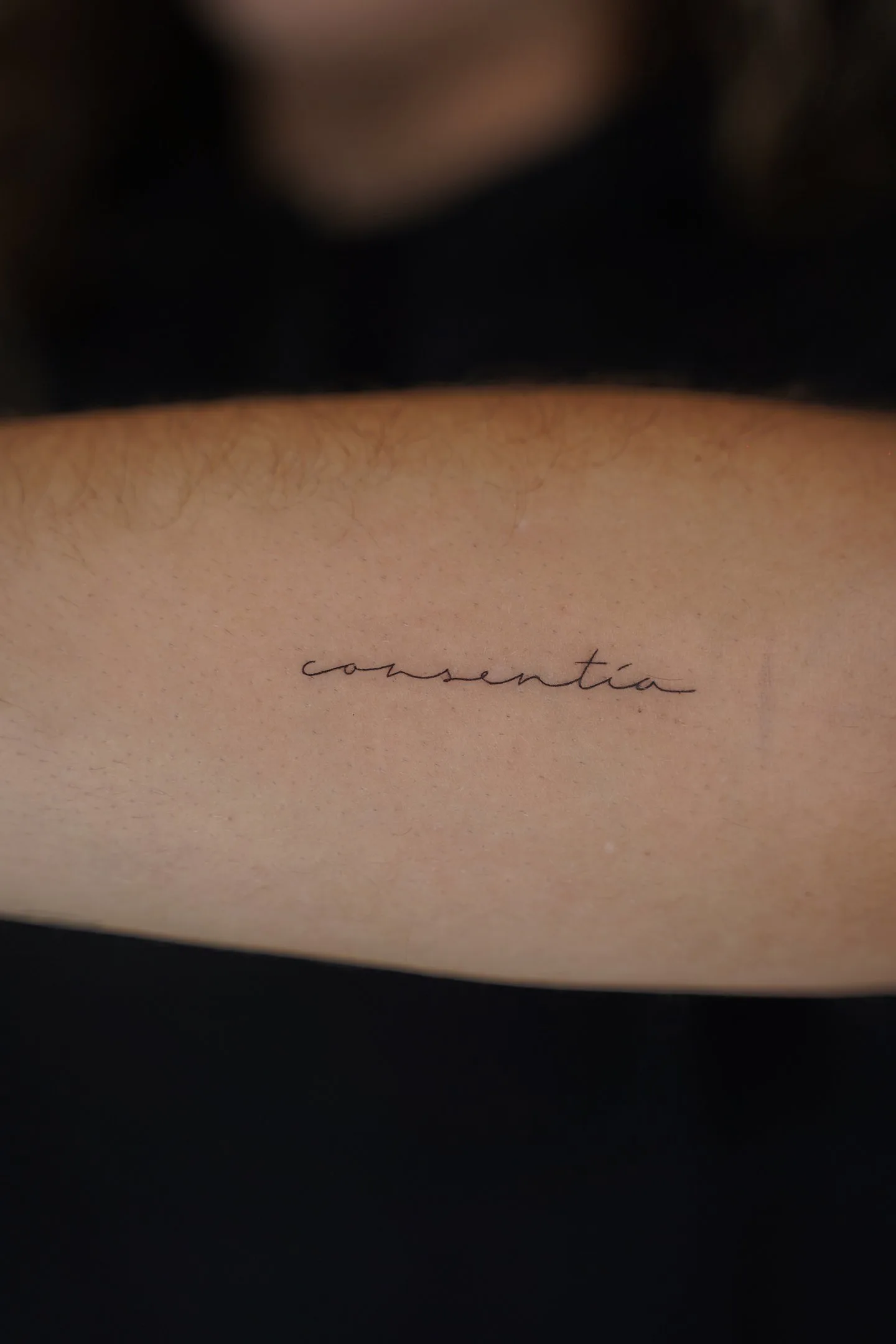 Tatuaje fineline palabra consentia en cursiva en brazo madrid