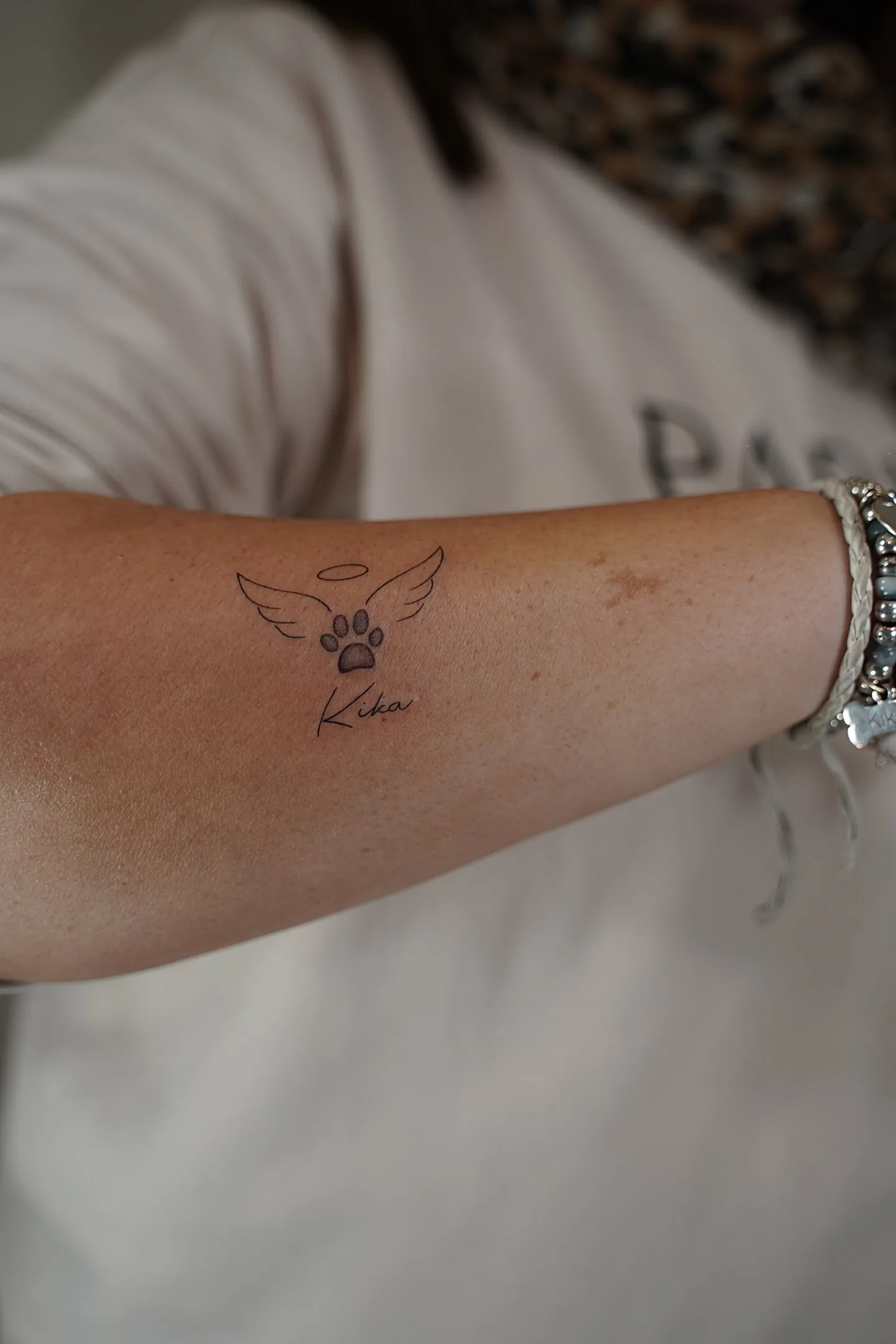 Tatuaje fineline huella de mascota con alas y nombre Kika en antebrazo madrid
