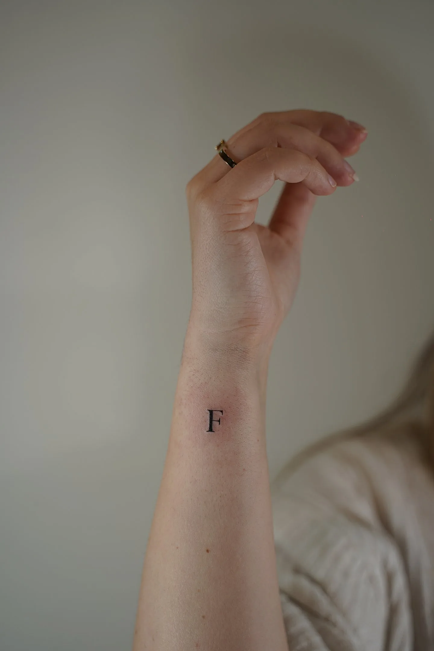 Tatuaje fineline letra F minimalista en muñeca madrid