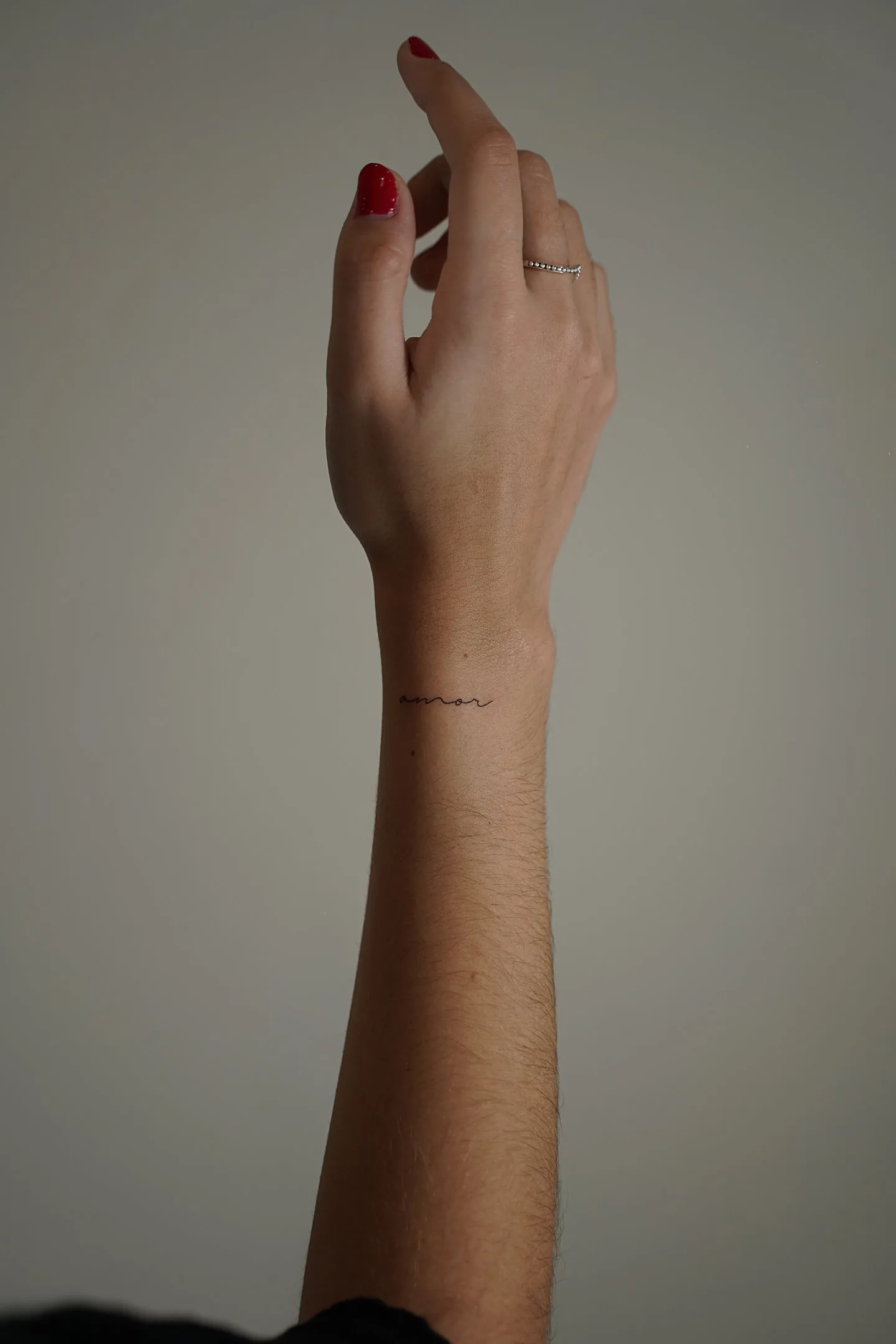 Tatuaje fineline palabra amor en cursiva minimalista en muñeca madrid