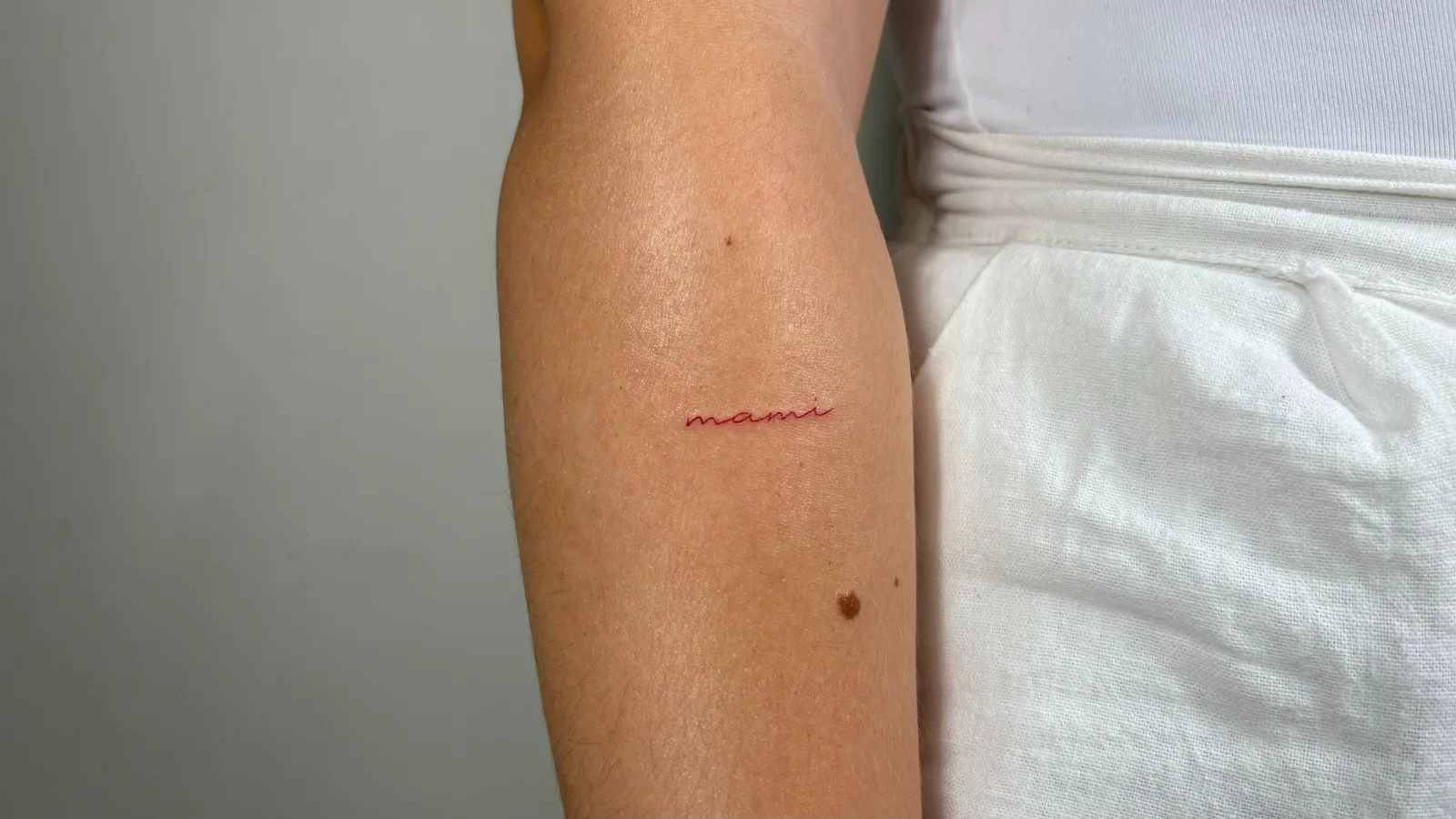 37) "Mami" en cursiva roja en el antebrazo