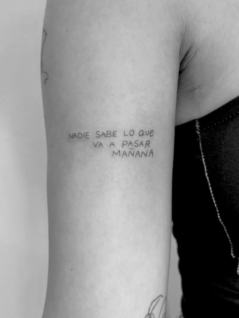 Fine line lettering tattoo “Nadie sabe lo que va a pasar mañana” (Bad Bunny) in typewriter type on the upper arm — Sinkply Madrid