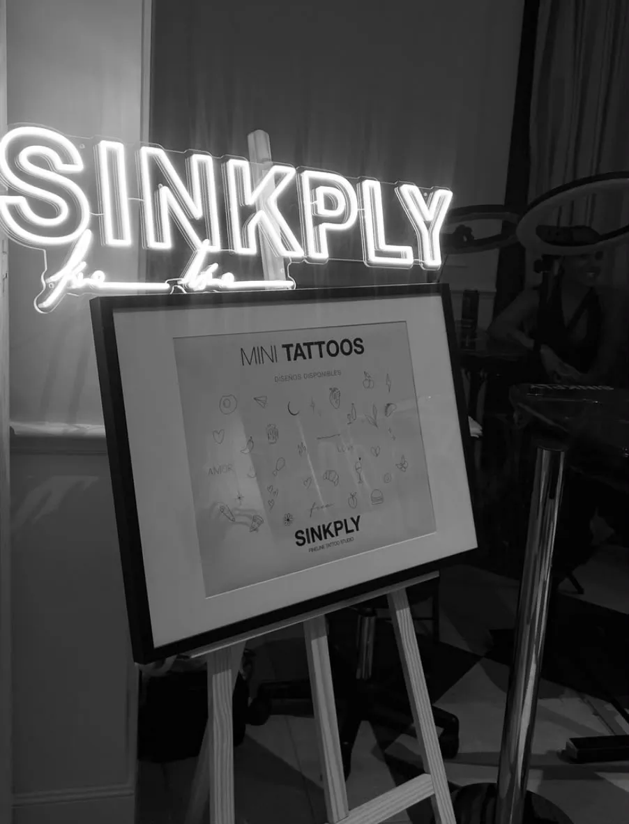 Cartel de neón de Sinkply junto al panel de mini tatuajes disponibles en una boda