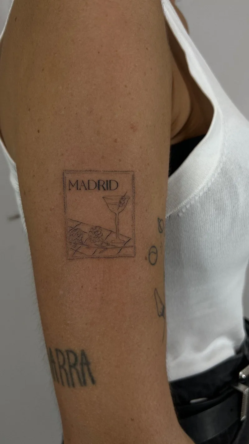 Tatuaje fine line con la palabra Madrid y una copa, en el brazo, en Sinkply Madrid