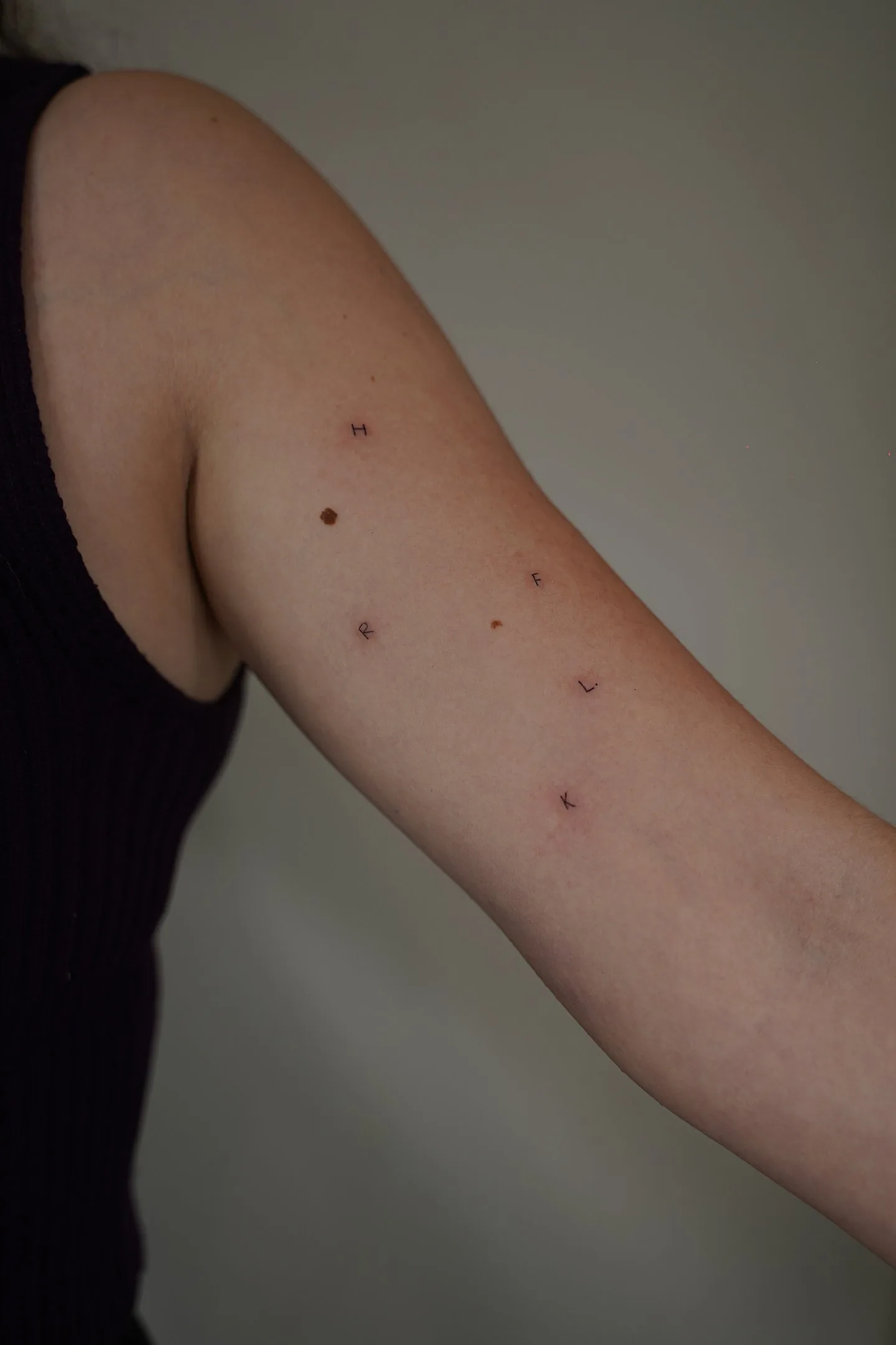 Scattered fine line initials H F C L K freckle tattoos on the arm — Sinkply Madrid