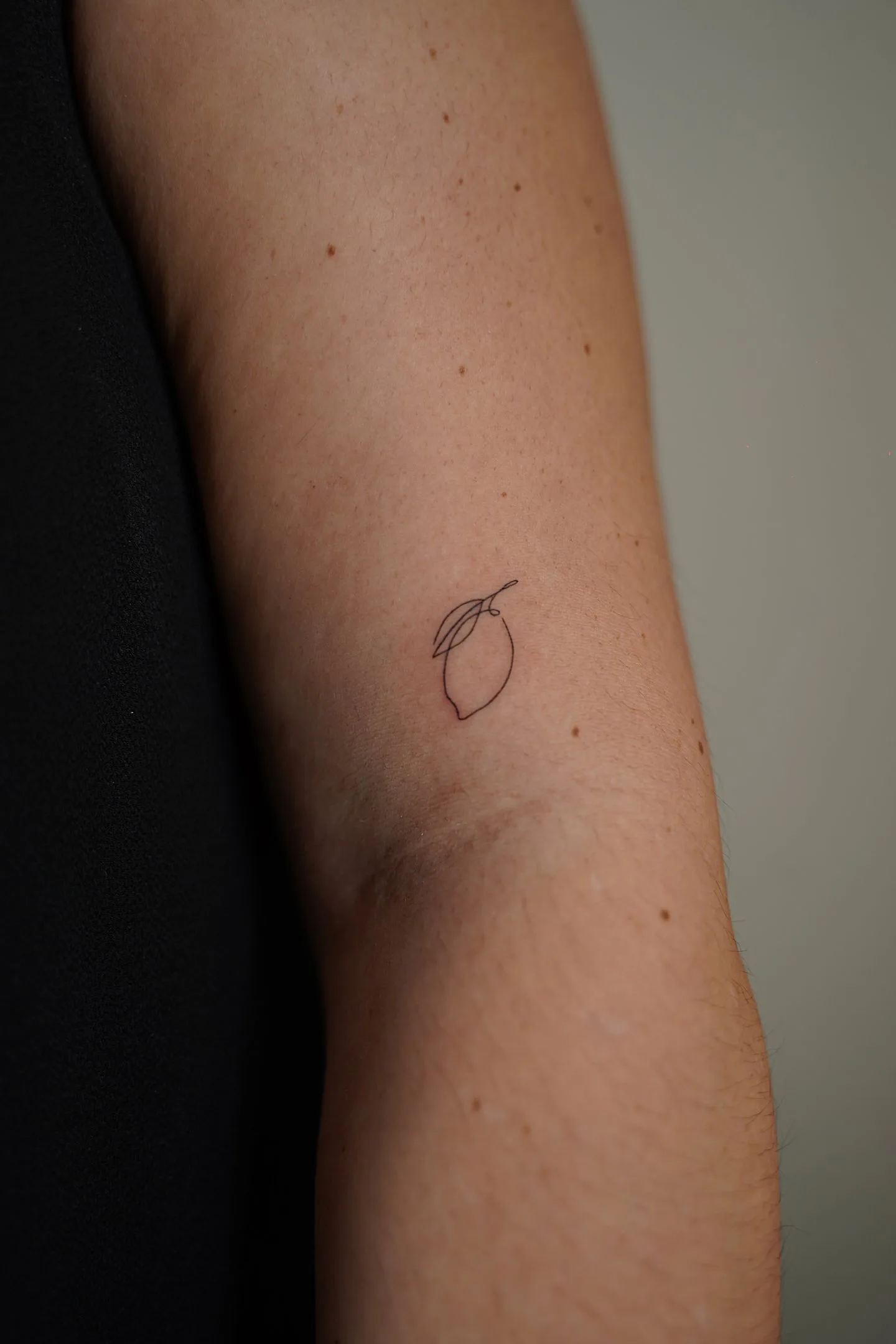 Fine line tattoo Madrid — minimalist lemon with leaf on the forearm