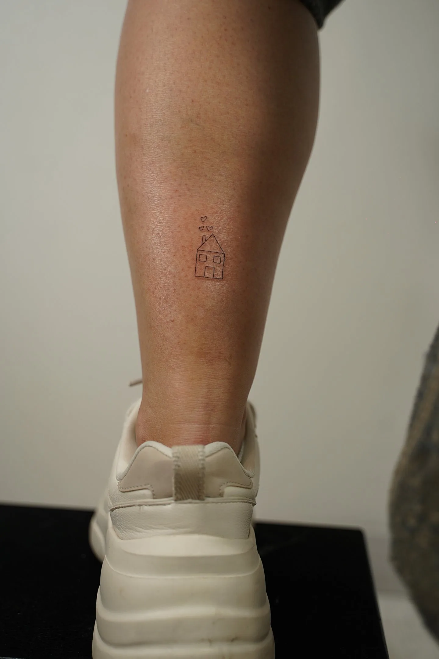 Fine line tattoo Madrid — small house with floating hearts on the thigh