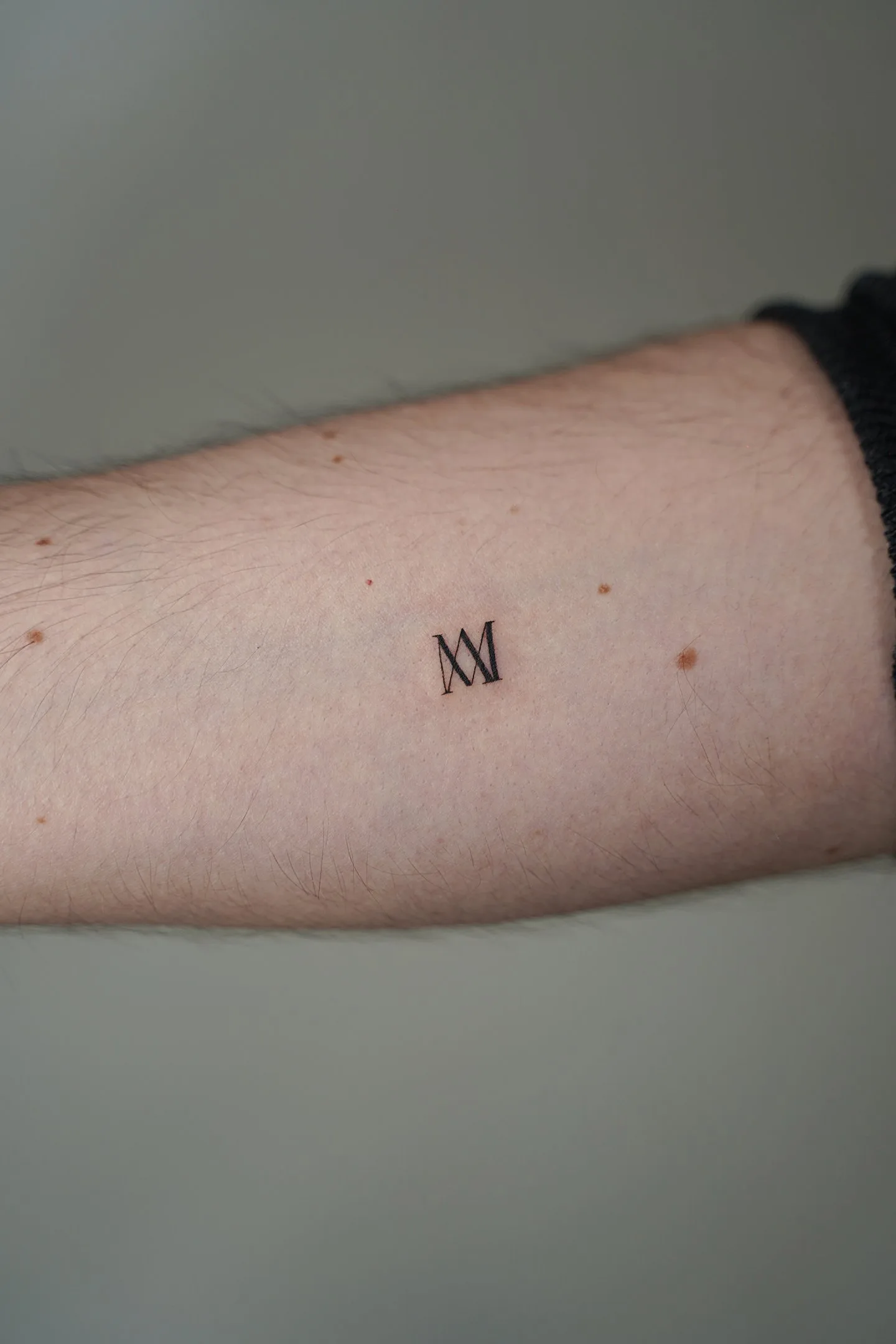 Fine line tattoo Madrid — MM initials in elegant serif on the forearm