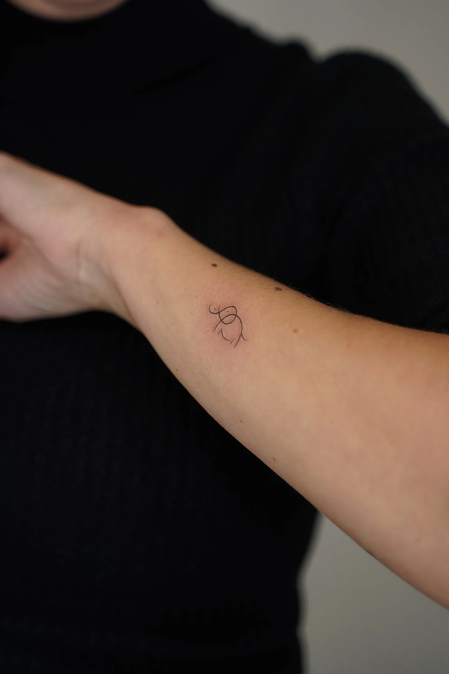 Fine line tattoo Madrid — gestural abstract figure on the forearm