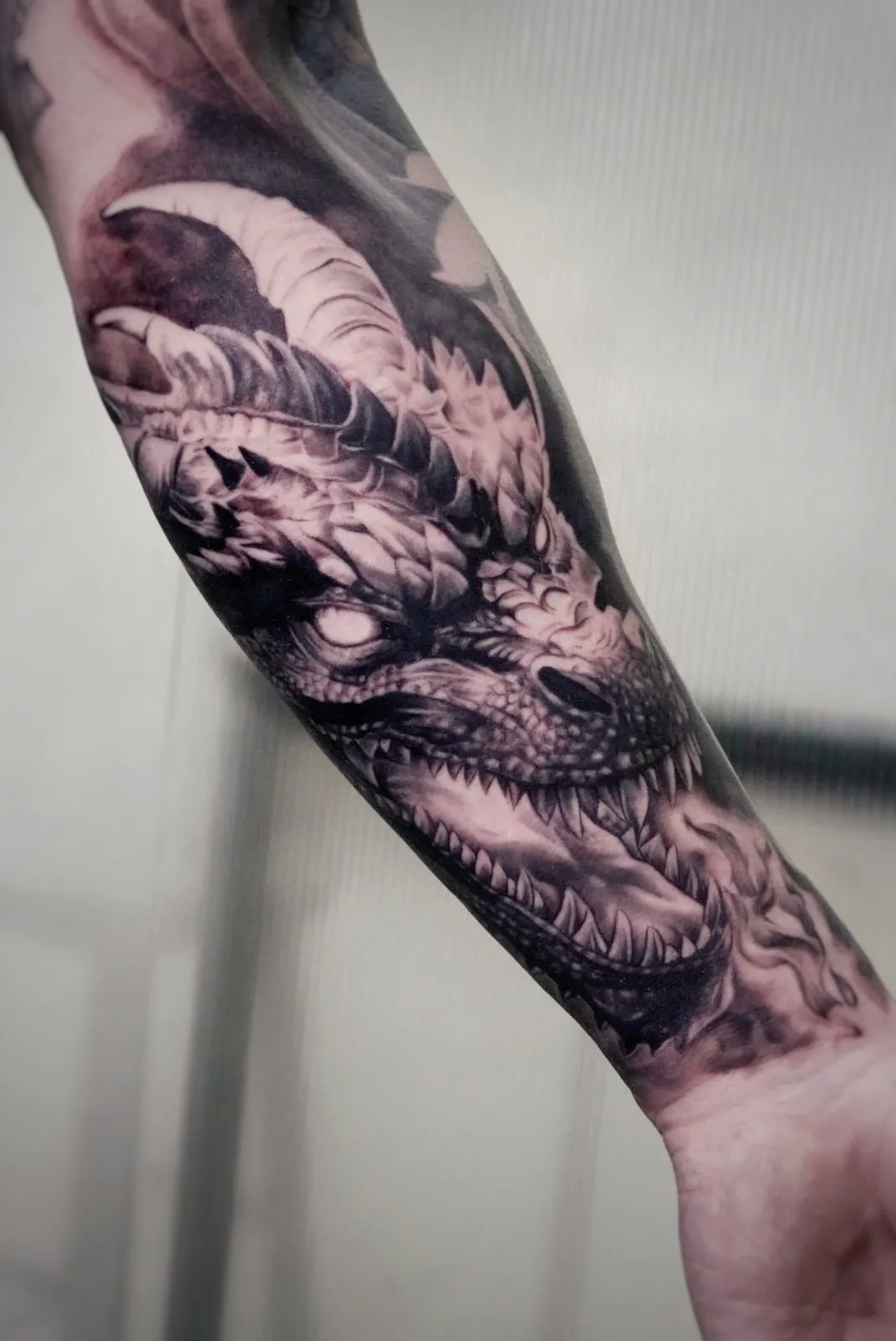 Tatuaje realismo cabeza de dragón con cuernos y escamas en antebrazo madrid