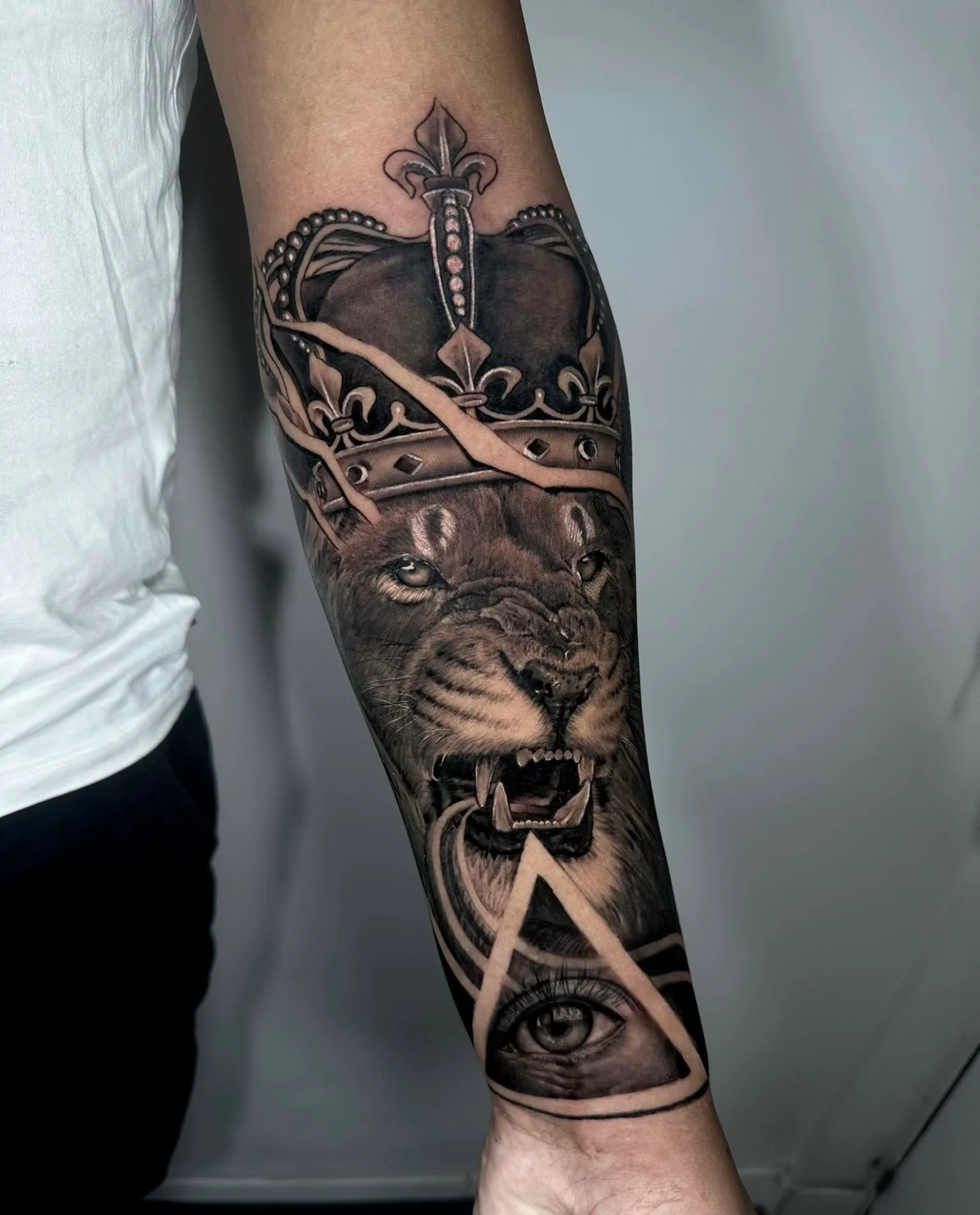 Tatuaje realismo león con corona y triángulo masónico en antebrazo madrid