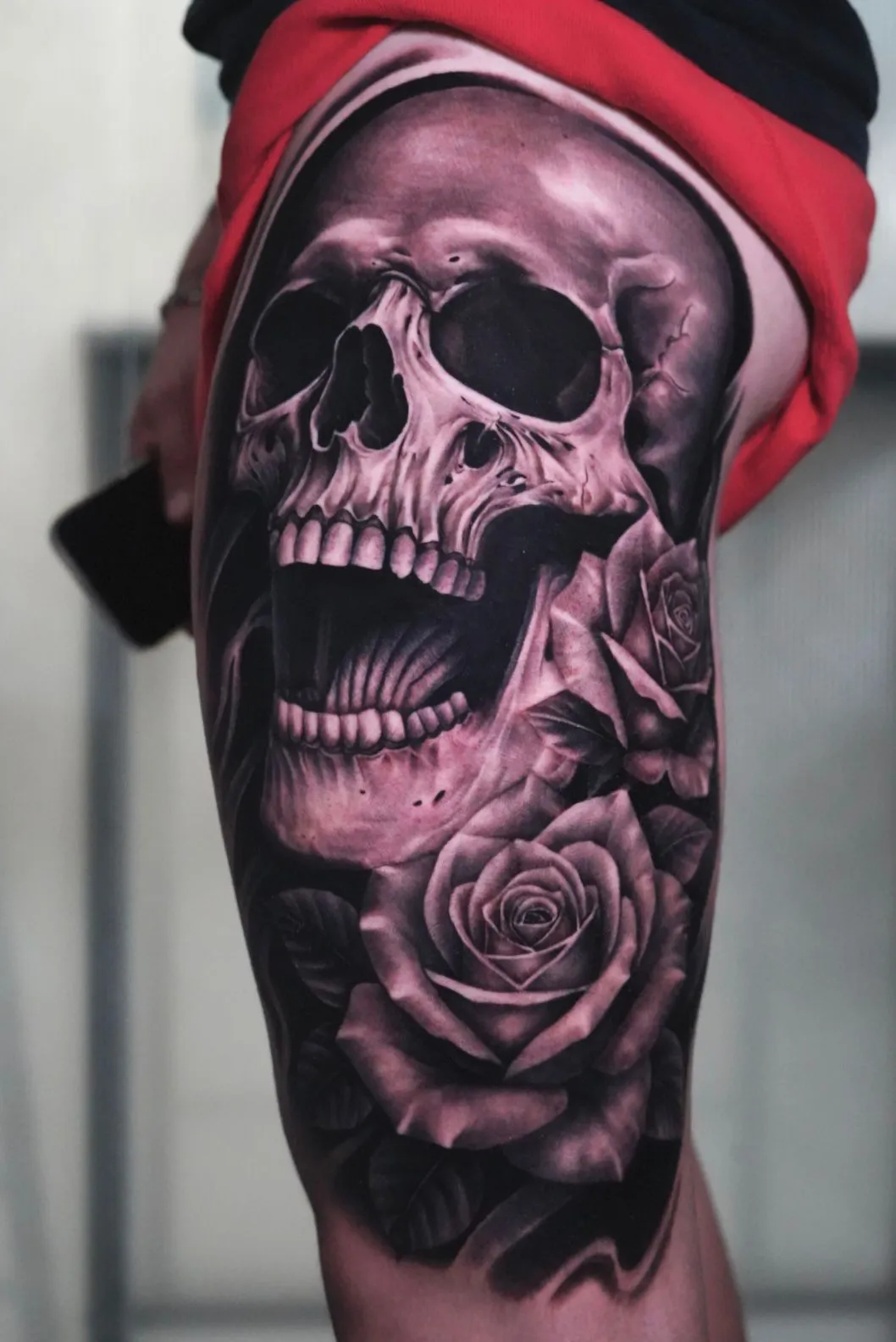 Tatuaje realismo calavera con boca abierta y rosas en muslo madrid
