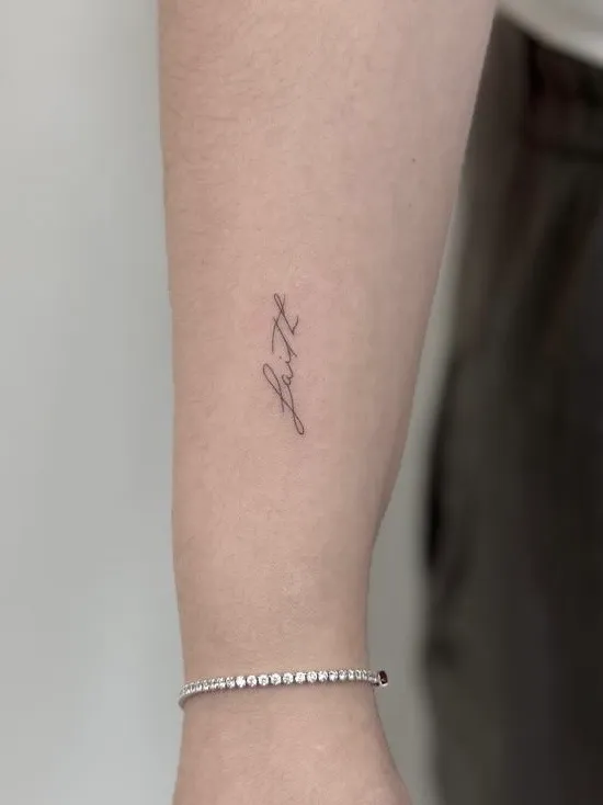Tatuaje de lettering manuscrito fino de una palabra en el antebrazo, por Oriana en Sinkply Madrid