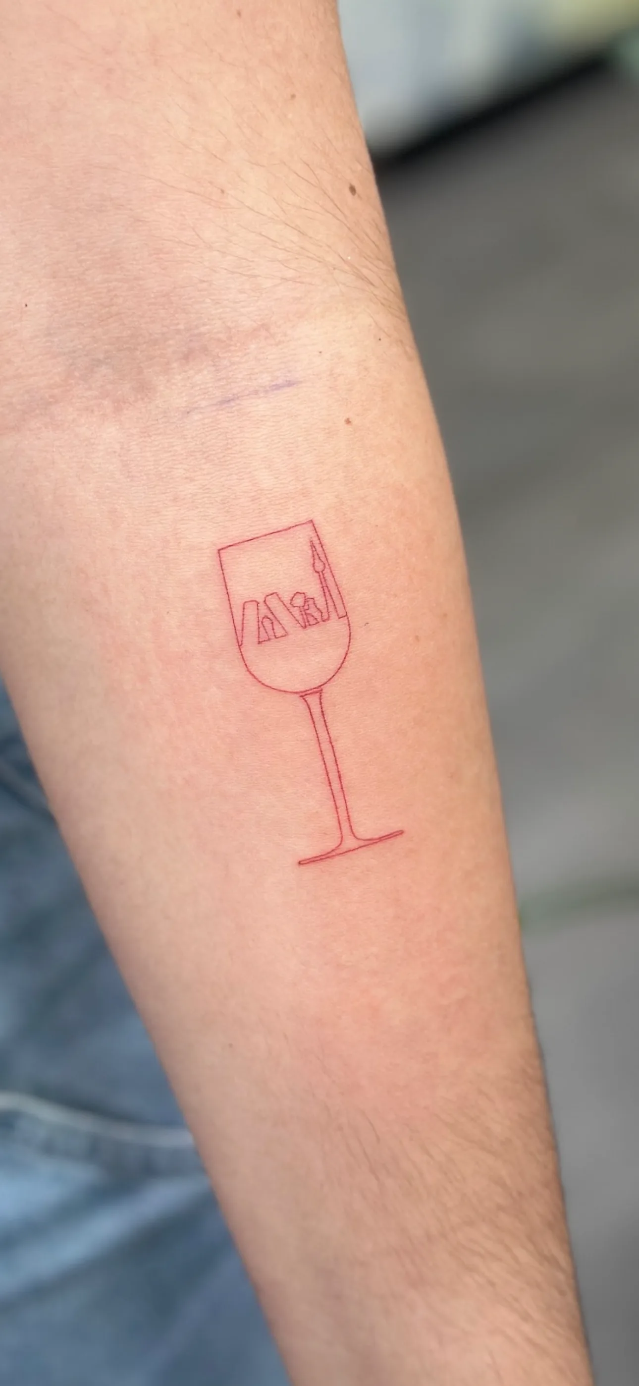 Fine line tattoo of a wine glass with the Madrid skyline inside, a souvenir of a trip to Madrid