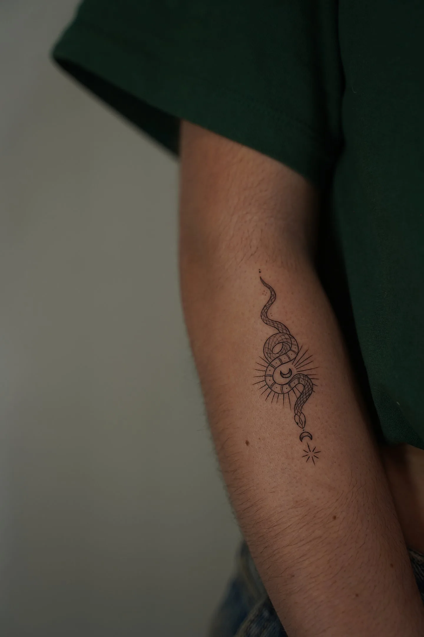 Tatuaje fineline en Madrid de serpiente mística enroscada en sol radiante con luna creciente