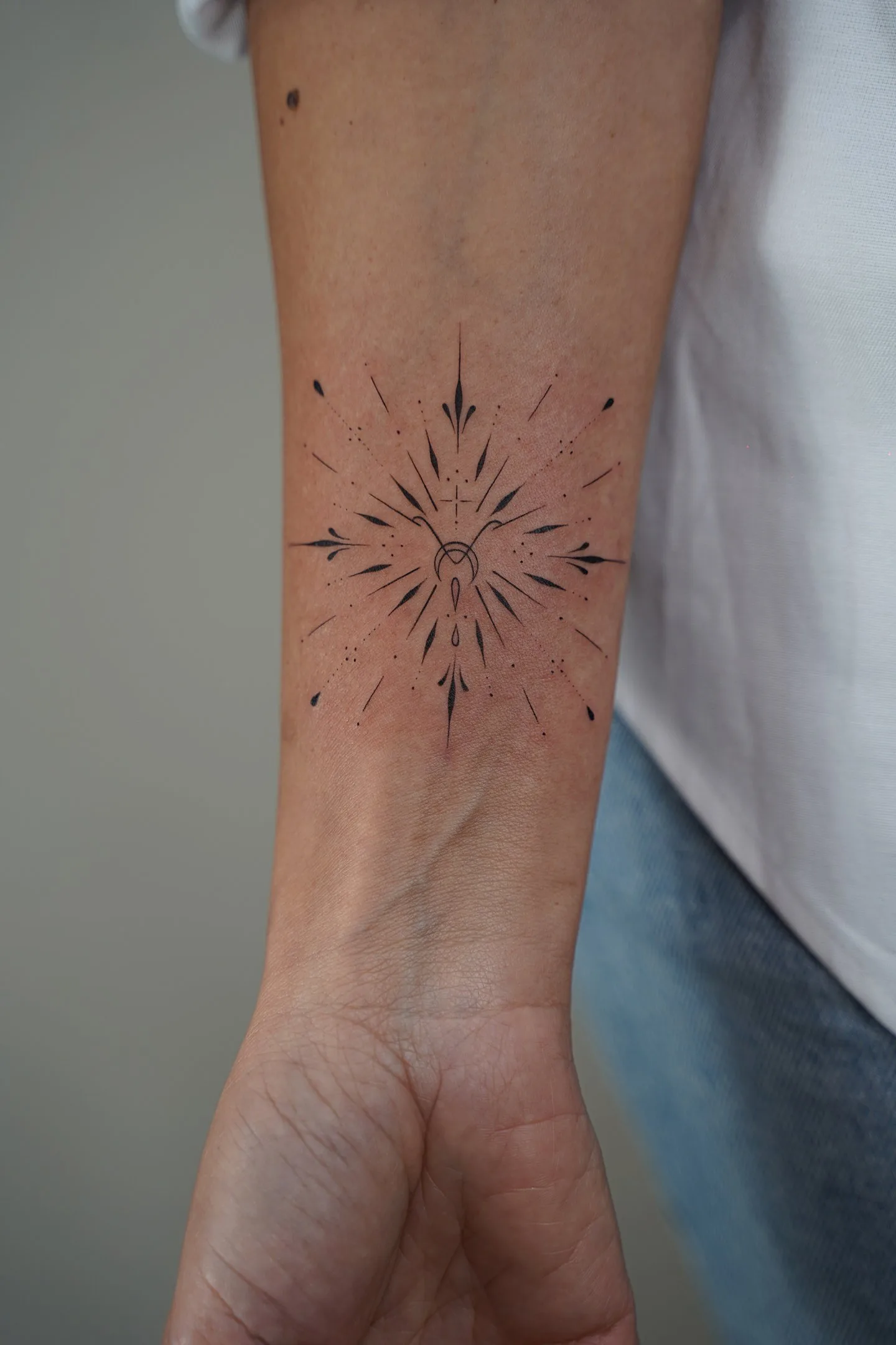 Tatuaje fineline ornamental en Madrid de estrella radiante simétrica con luna creciente cruz y detal