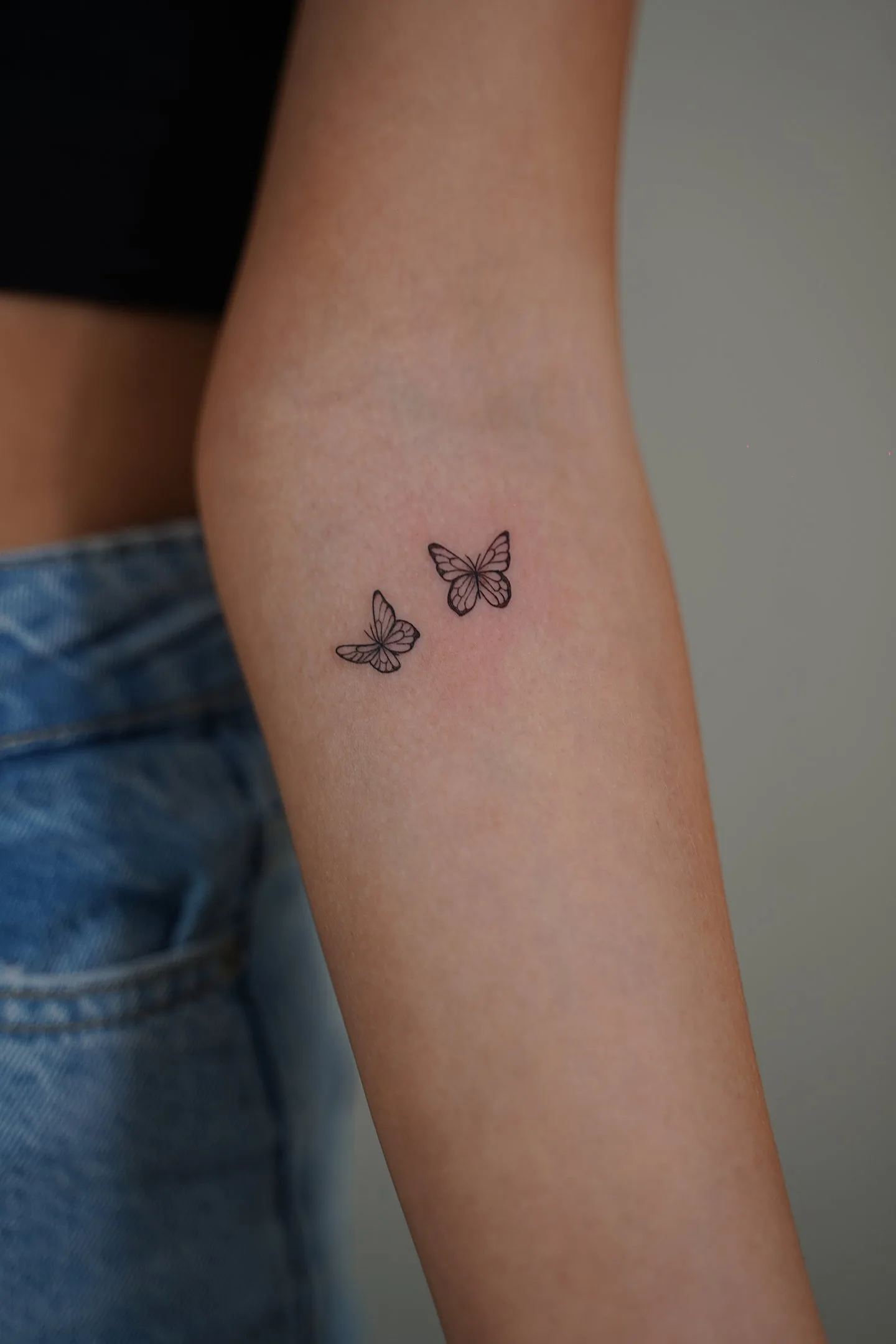 Tatuaje fineline en Madrid de dos mariposas pequeñas en vuelo con trazo delicado en el antebrazo