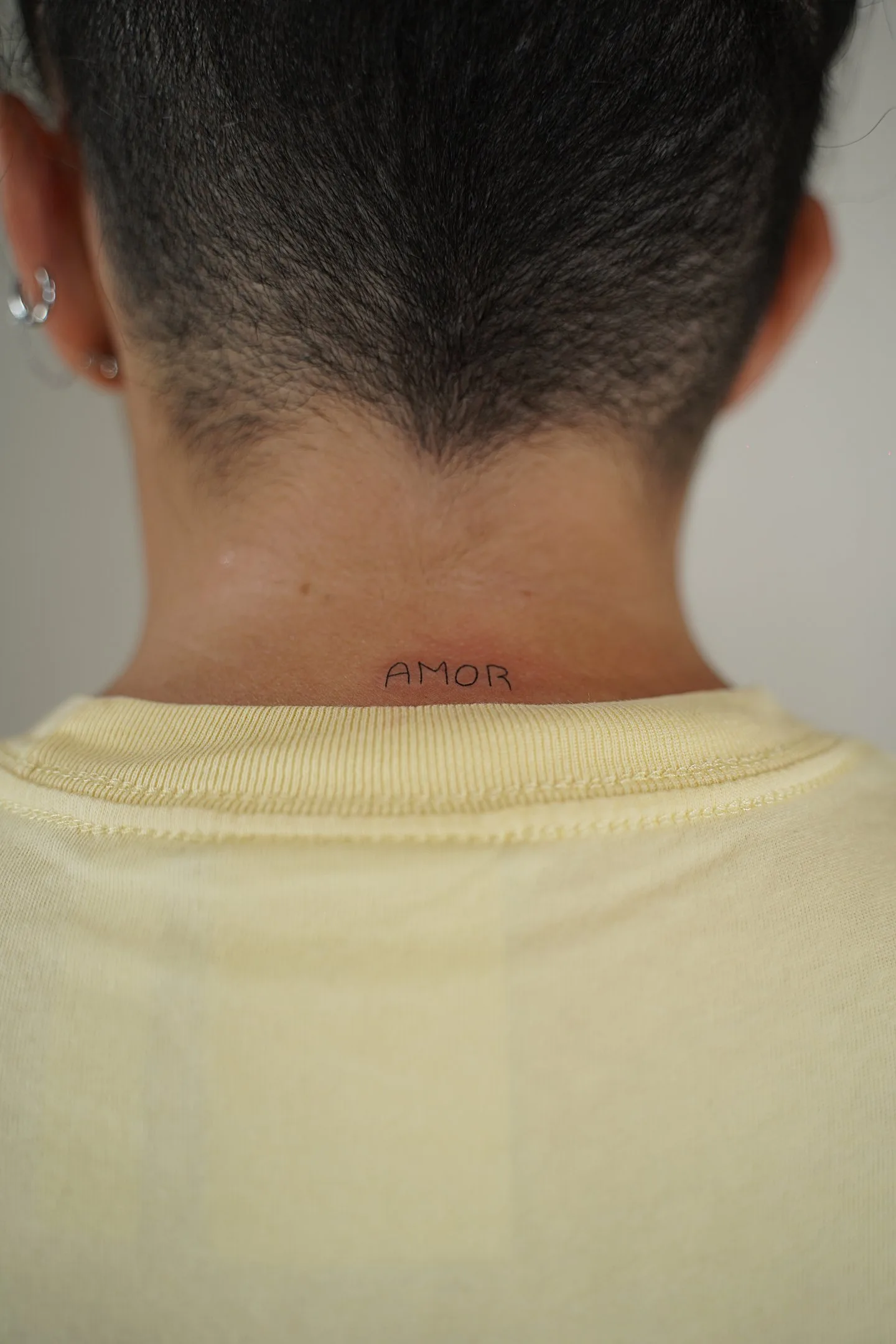 Fine line tattoo Madrid — AMOR lettering in capitals on the nape