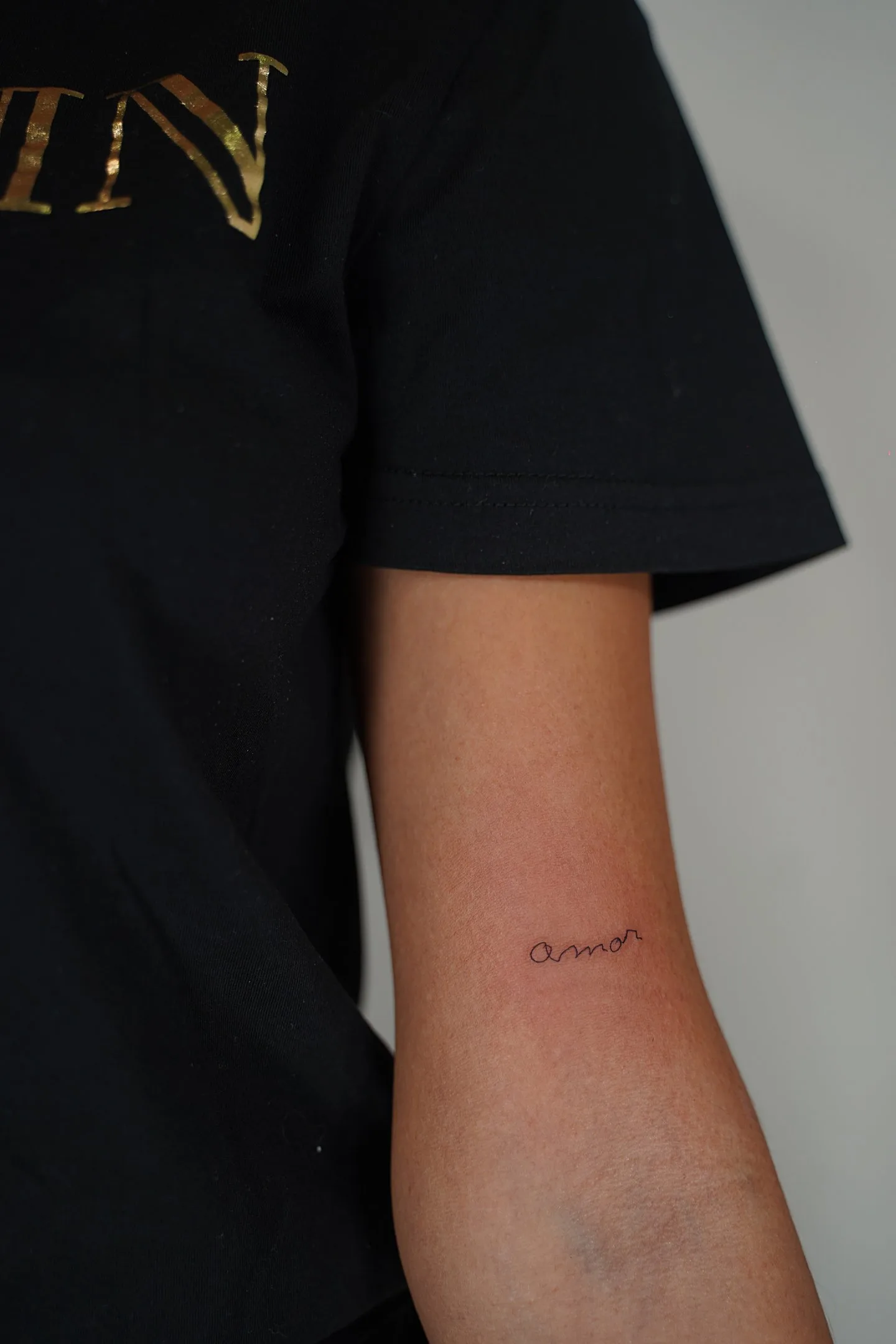 Fine line tattoo Madrid — amor in lowercase cursive fine line on the forearm