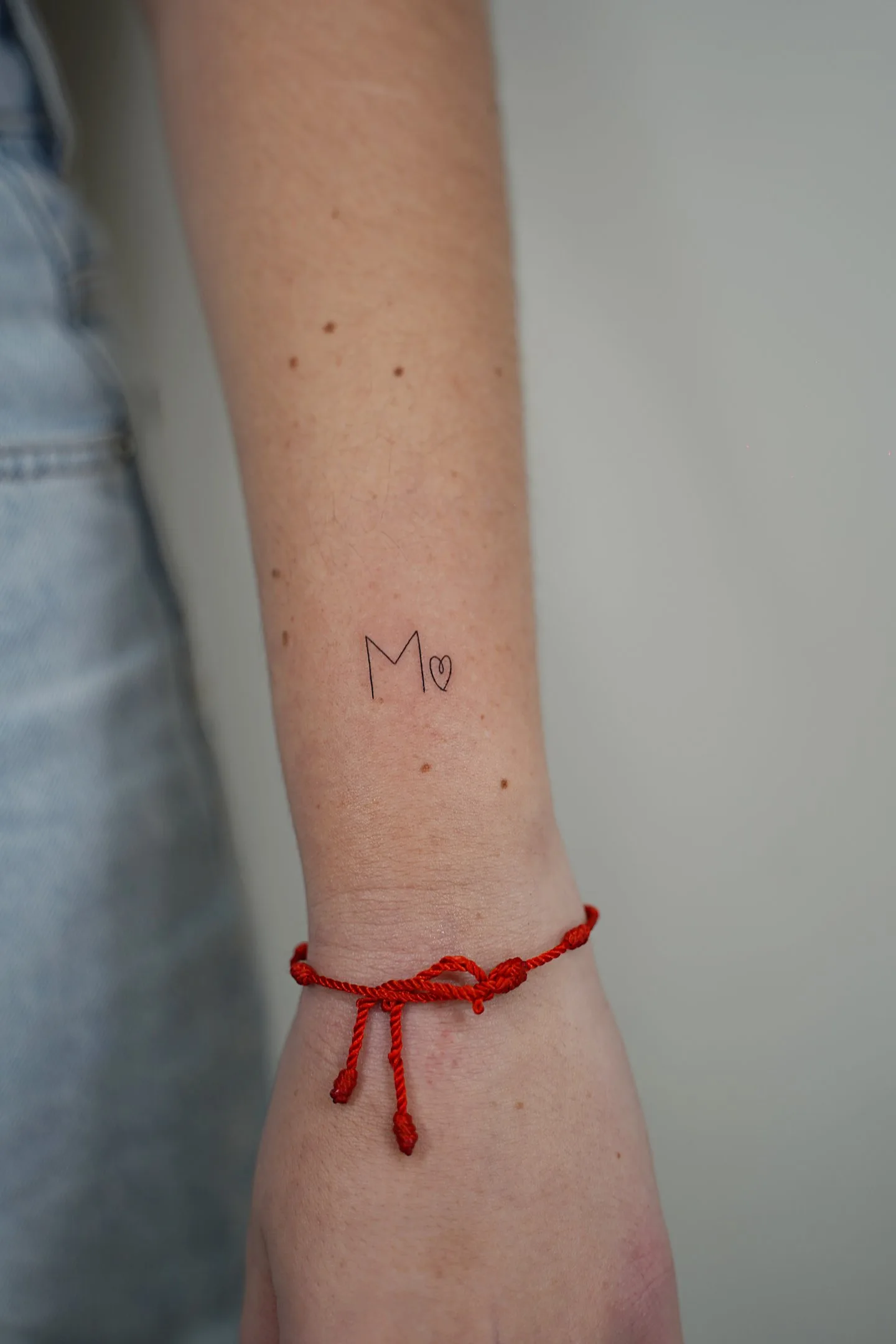 Fine line tattoo Madrid — initial M with small heart on the wrist