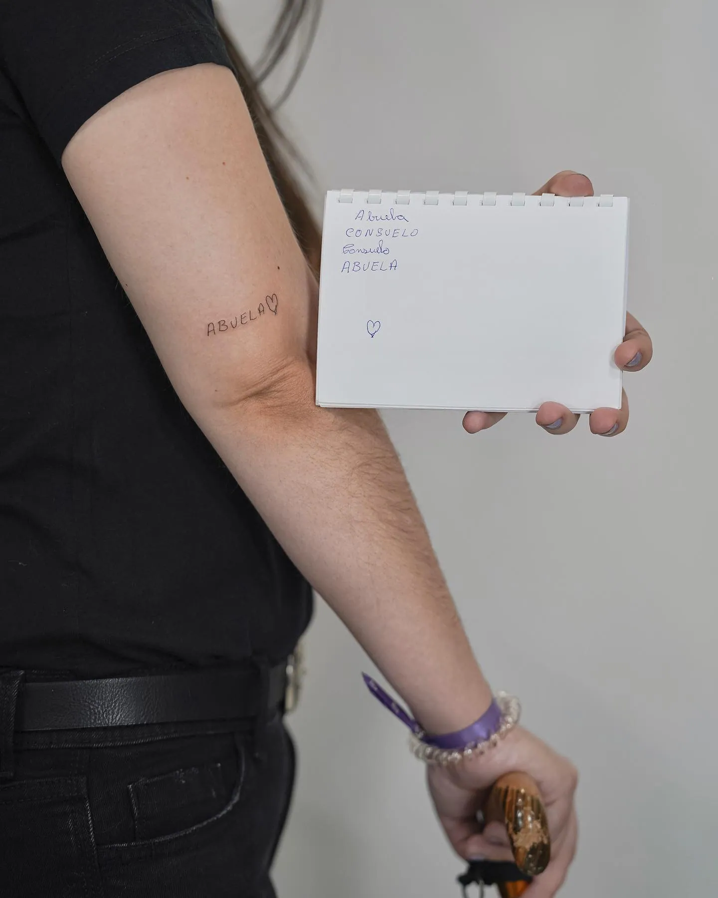 Fine line tattoo Madrid — the word ABUELA with a heart on the forearm, next to the notebook with the original handwriting
