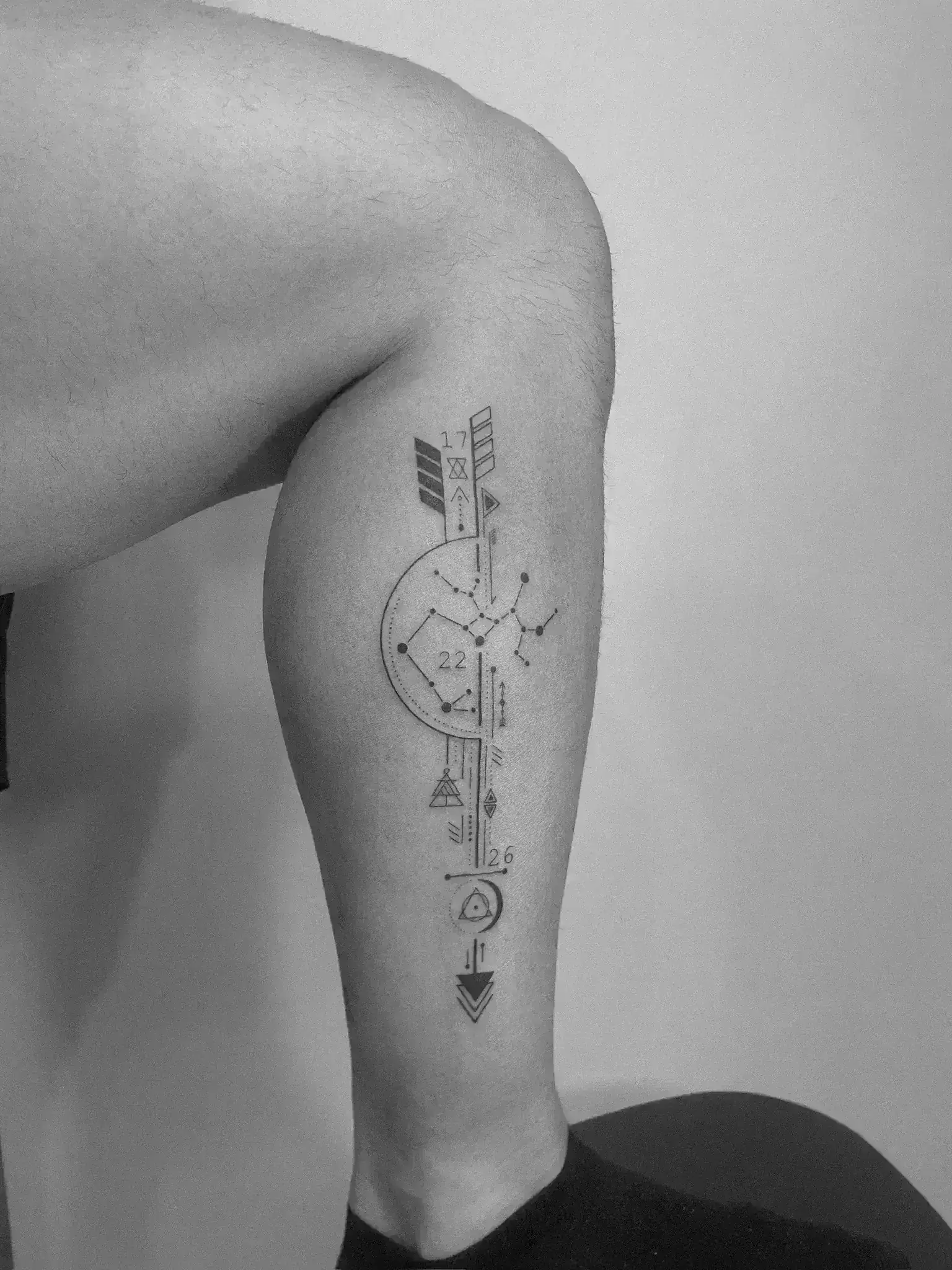 Tatuaje geométrico flecha con constelación y símbolos en pierna madrid