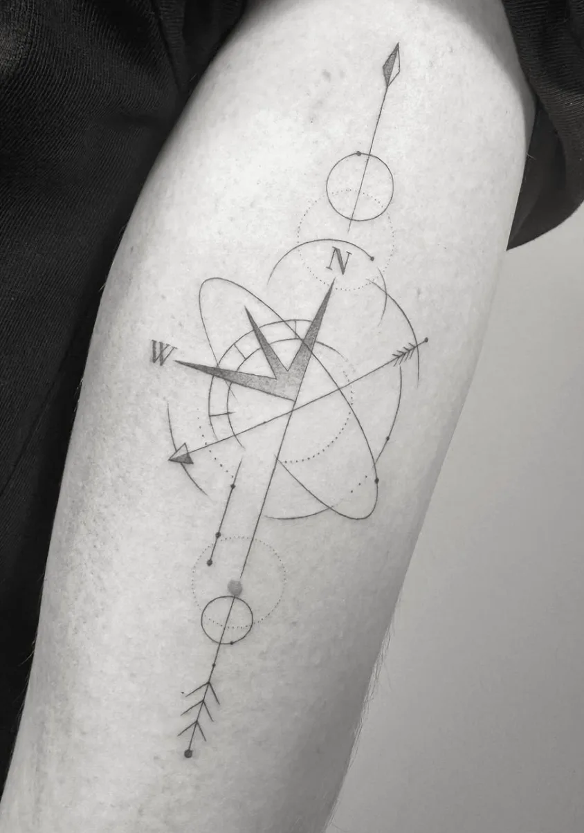 Tatuaje fineline brújula geométrica con átomo y flechas en antebrazo madrid